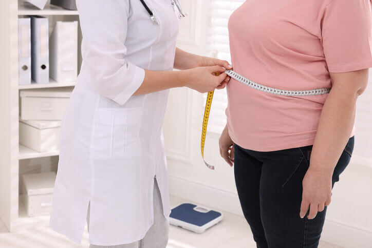 Nutritionist measuring overweight woman's waist with tape in clinic