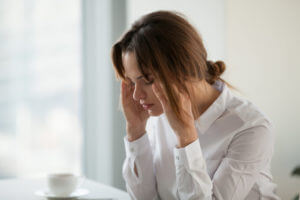 A tired and exhausted businesswoman is feeling a strong headache at work due to hormonal imbalances.