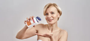 A middle-aged Caucasian woman smiles at the camera while pouring pills resembling Rapamycin from a bottle to illustrate anti-aging and longevity.