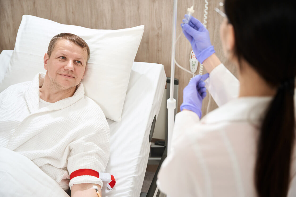 A male patient is lying in a hospital bed while receiving infusion therapy.