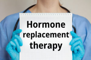 A female healthcare provider holds a journal inscribed with Hormone Replacement Therapy.