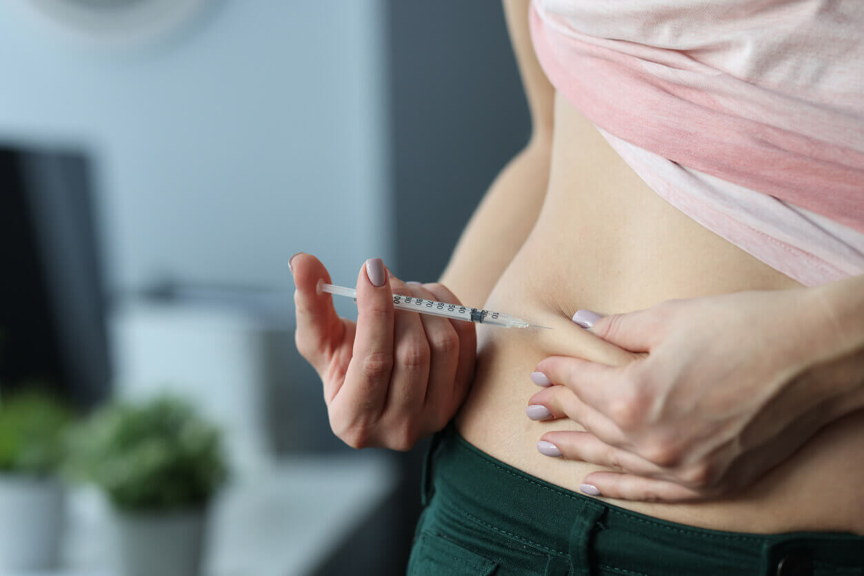 A woman is making a skin fold on her stomach and injecting a weekly weight loss injection from a syringe at home.