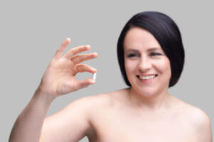 A woman is holding a white pill in hand, which is a testosterone pellet for women.