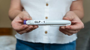 GLP-1 injection pen held by woman in front of abdomen, weight management concept.