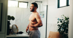 Happy man, belly and weightloss in bathroom for personal care or self confidence at home.