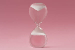 Upside-down hourglass on pink background - Concept of reverse aging.