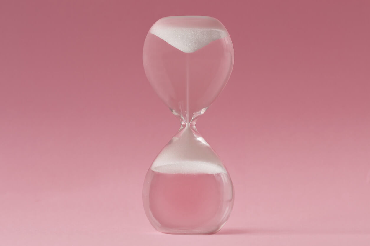Upside-down hourglass on pink background - Concept of reverse aging.